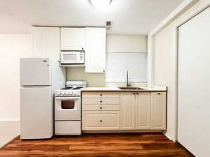 Kitchen featuring white appliances, light countertops, dark wood-type flooring, and white cabinets