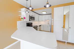 Kitchen featuring stainless steel appliances, white cabinets, decorative light fixtures, and open shelves