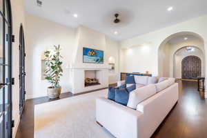 Living area with a fireplace, arched walkways, dark wood-style floors, ceiling fan, and recessed lighting