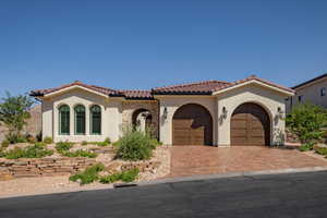 Mediterranean / spanish-style house with stucco siding, an attached garage, decorative driveway, and stone siding