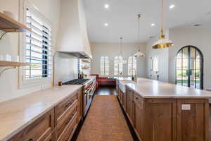 Kitchen featuring a large island with sink, open shelves, range with two ovens, and wood finish cabinets