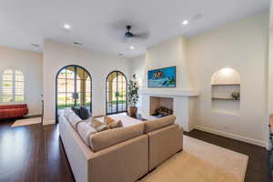 Living area with built in features, dark wood-type flooring, ceiling fan, recessed lighting, and a fireplace