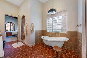 Ensuite bathroom with a soaking tub, tile walls, wainscoting, and dark tile patterned flooring