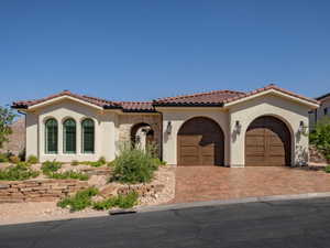 Mediterranean  home with stucco siding, driveway, a tiled roof, and a garage