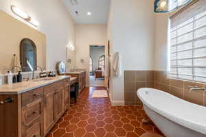 Full bathroom with two vanities, a freestanding tub, tile walls, and wainscoting