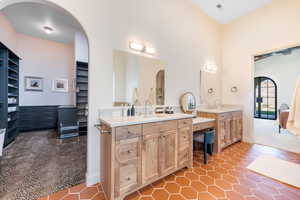 Full bathroom featuring two vanities, connected bathroom, a spacious closet, a high ceiling, and dark tile patterned floors