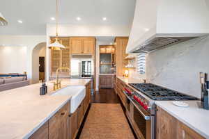 Kitchen with range with two ovens, tasteful backsplash, light stone countertops, wood finish cabinets, and decorative light fixtures