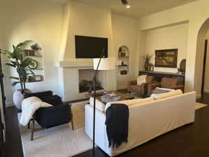 Living room featuring built in features, a fireplace, wood finished floors, arched walkways, and recessed lighting