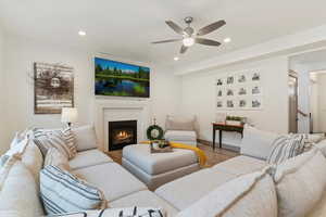 Living room featuring wood finished floors, a stone fireplace, ceiling fan, and recessed lighting