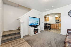 Living room with light wood-type flooring, arched walkways, light colored carpet, a warm lit fireplace, and a textured ceiling
