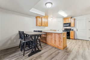 Kitchen with a peninsula, black appliances, light wood-type flooring, light wood finish cabinets, and a textured ceiling