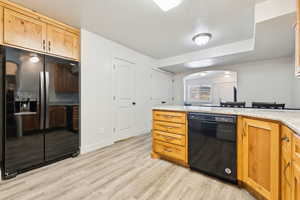 Kitchen featuring black appliances, light wood-type flooring, a textured ceiling, a peninsula, and light stone countertops