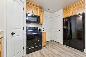 Kitchen featuring black appliances, light wood-style flooring, light wood finish cabinets, a textured ceiling, and light stone countertops