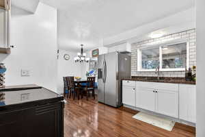 Kitchen featuring stainless steel fridge, backsplash, white cabinets, dark wood-style flooring, and a textured ceiling