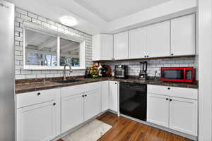 Kitchen featuring white cabinetry, dishwasher, dark wood finished floors, dark stone counters, and backsplash