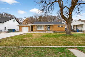 View of front facade featuring a front lawn, concrete driveway, a garage, and brick siding