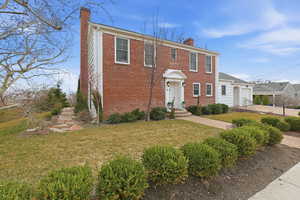 Colonial house featuring a chimney, brick siding, and a front lawn
