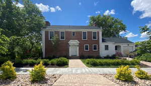Colonial home featuring a chimney, brick siding, and an attached garage