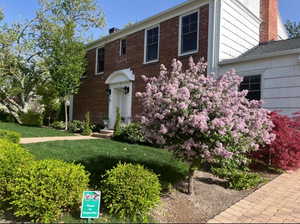 Colonial home featuring a chimney, a front lawn, and brick siding