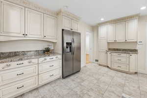 Kitchen featuring stainless steel fridge, cream cabinetry, dark stone countertops, and recessed lighting
