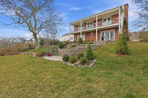 Back of property featuring a chimney, a lawn, brick siding, and a patio