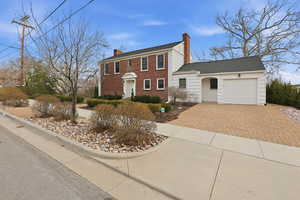 Colonial-style house with a chimney, decorative driveway, an attached garage, and brick siding