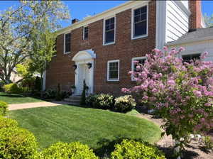 Colonial inspired home featuring a chimney, brick siding, and a front lawn