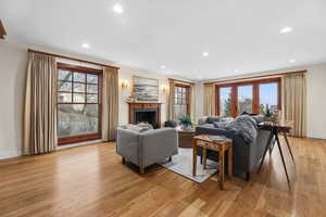 Living room with light wood-style flooring, a lit fireplace, recessed lighting, and french doors