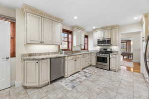 Kitchen with cream cabinets, stainless steel appliances, healthy amount of natural light, light stone countertops, and recessed lighting