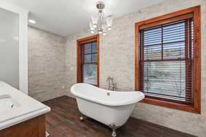 Bathroom featuring a freestanding tub, double vanity, hanging lights, dark wood-style floors, and tile walls