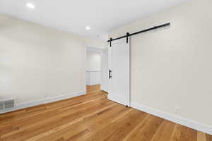 Empty room featuring a barn door, light wood-type flooring, and recessed lighting