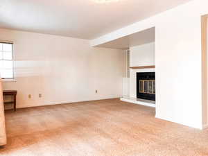 Unfurnished living room featuring light carpet, a glass covered fireplace, and built in shelves