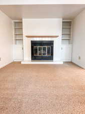 Unfurnished living room with built in shelves, a fireplace, and carpet floors