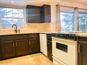 Kitchen with white appliances, light stone counters, and backsplash