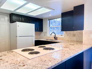 Kitchen featuring white appliances, light stone countertops, tasteful backsplash, dark cabinets, and blue cabinets