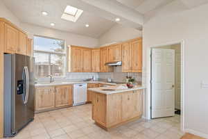 Kitchen with light wood finish cabinetry, stainless steel refrigerator with ice dispenser, light countertops, a skylight, and recessed lighting