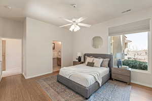 Bedroom with light wood-style flooring, ensuite bathroom, and ceiling fan