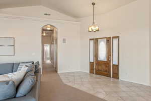Entrance foyer featuring light tile patterned floors, arched walkways, vaulted ceiling, light colored carpet, and suspended lighting
