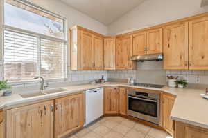 Kitchen with oven, light wood finish cabinets, white dishwasher, decorative backsplash, and lofted ceiling