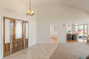 Foyer entrance featuring hanging lights, light tile patterned floors, a high ceiling, and light carpet