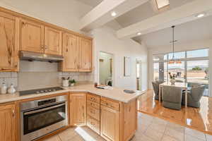 Kitchen featuring stainless steel oven, light countertops, tasteful backsplash, light tile patterned flooring, and lofted ceiling