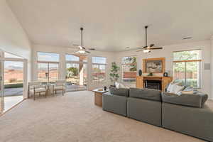 Living room with a ceiling fan, light colored carpet, a fireplace, and lofted ceiling