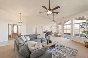 Living area with light colored carpet, a ceiling fan, suspended lighting, and lofted ceiling