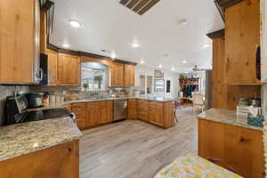 Kitchen with a peninsula, wood finish cabinetry, range with electric stovetop, light stone counters, and a ceiling fan