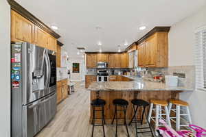 Kitchen with stainless steel appliances, a peninsula, a breakfast bar, light stone counters, and light wood-style flooring