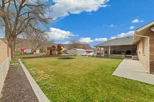 View of grassy yard with a playground, a trampoline, a patio area, and a deck