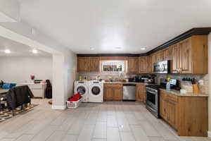 Kitchen with stainless steel appliances, wood finish cabinets, light stone counters, separate washer and dryer, and backsplash