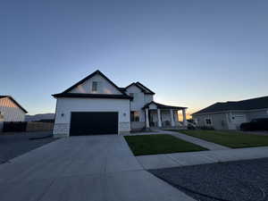 Modern farmhouse with a porch, driveway, stone siding, and an attached garage