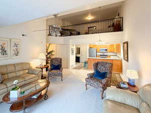 Living area featuring ceiling fan, light carpet, a chandelier, vaulted ceiling, and light tile patterned floors