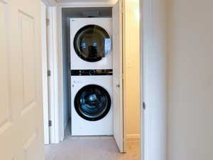 Laundry area with stacked washer and dryer and light carpet
